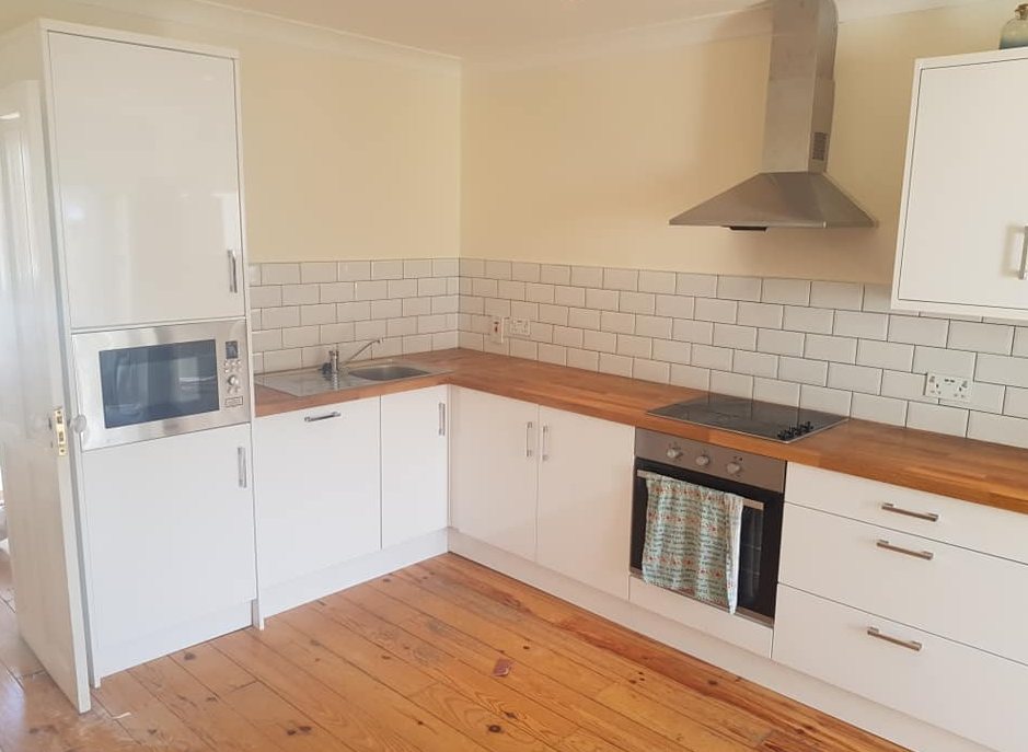 A white kitchen with a timber worktop and metro tiles over a pine floor