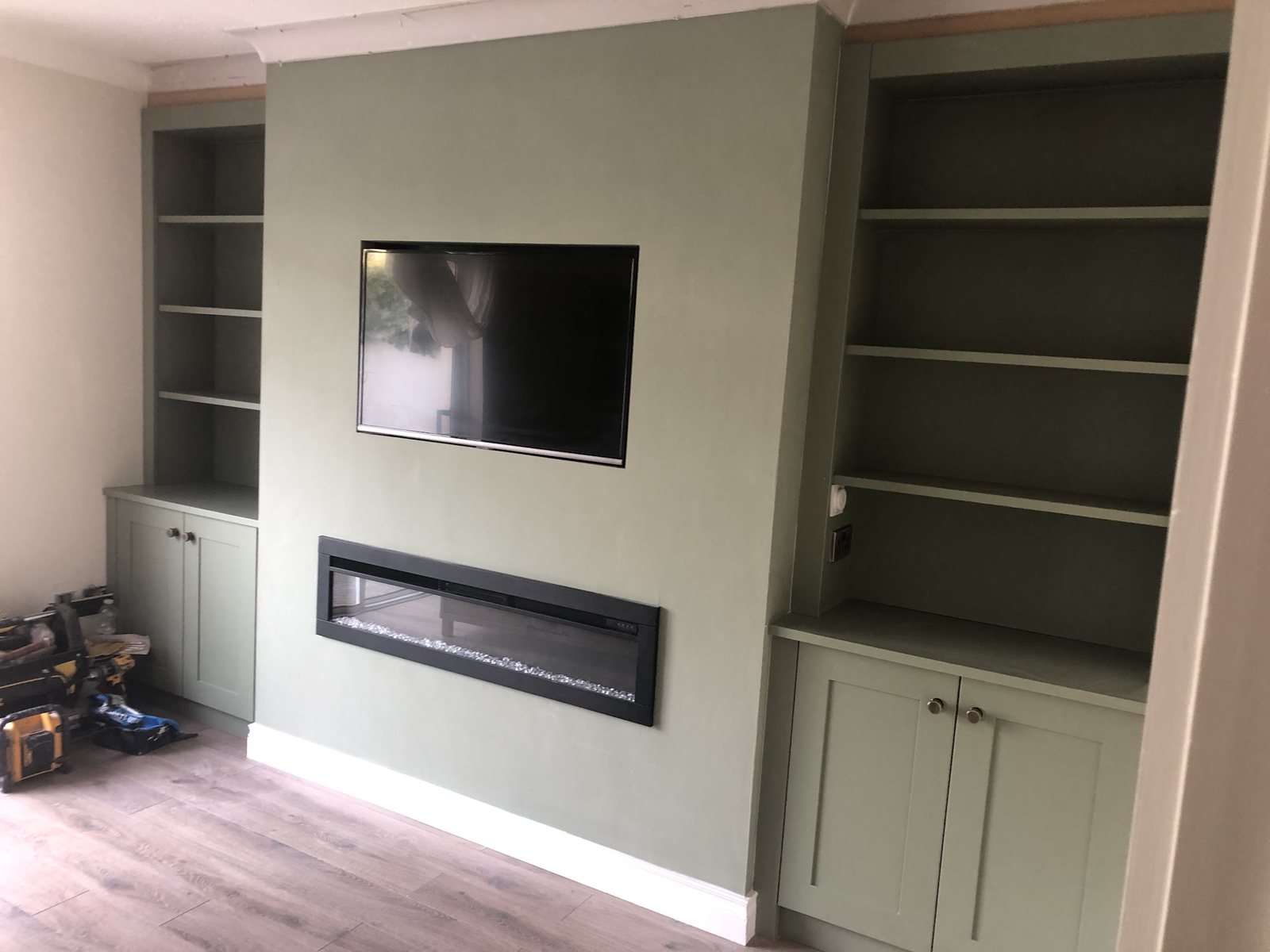 A media wall with a fire and TV between green alcove units with shelves