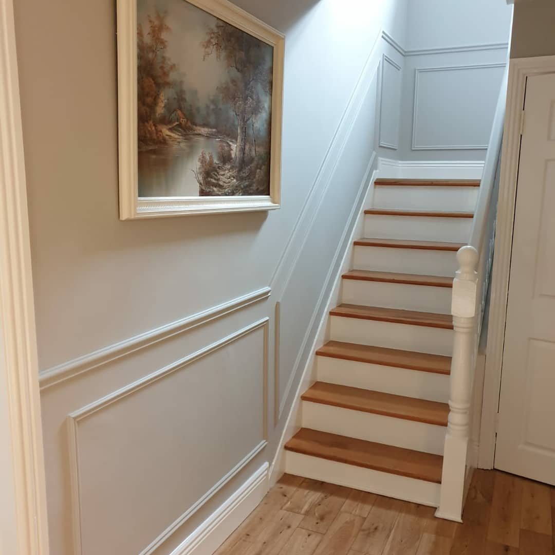 A staircase with timber treads beside a white panelled wall