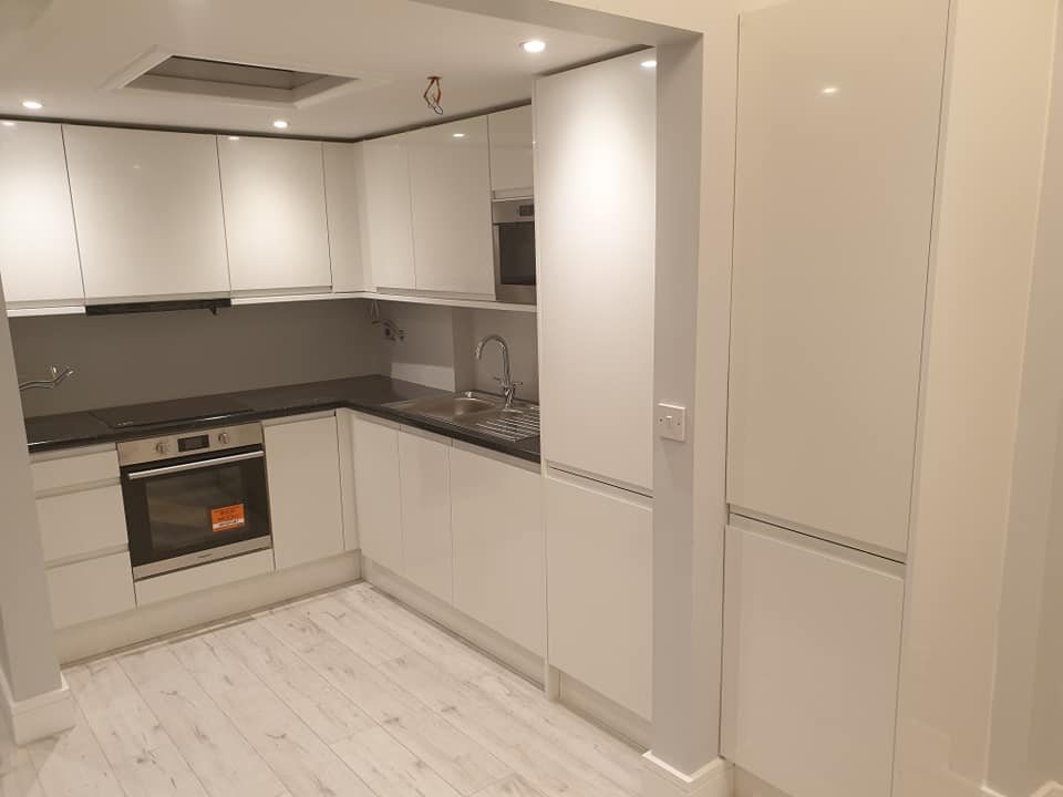 A white gloss kitchen with a grey worktop and built-in oven