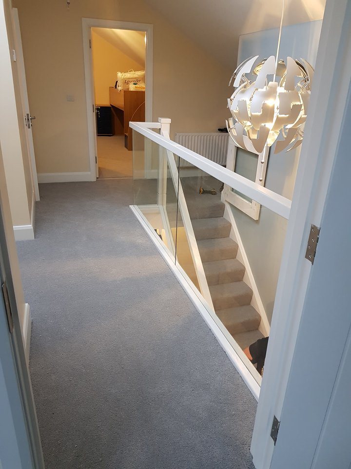 A landing with a glass balustrade above the stairs and a bedroom door open beyond