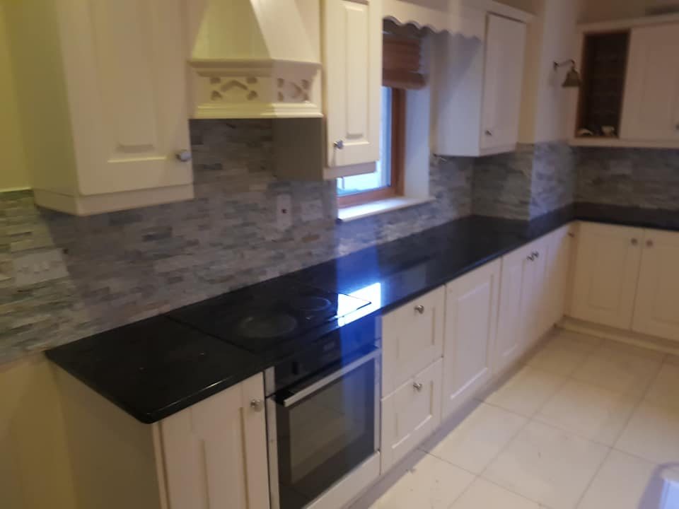 A cream kitchen with a black granite worktop and mosaic splashback
